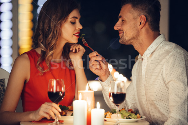 Smiling careful man feed his pretty girlfriend while have romantic dinner at home Stock photo © deandrobot