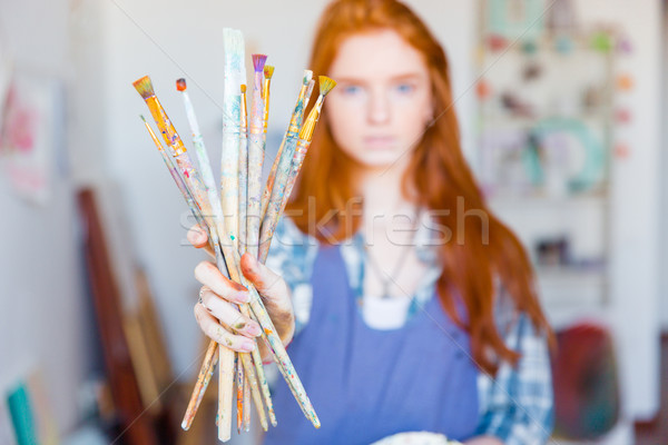 Young woman painter showing dirty paintbrushes in artist workshop Stock photo © deandrobot