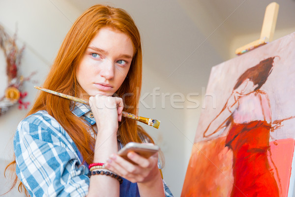 Thoughtful attractive woman painter thinking and holding cellphone in workshop Stock photo © deandrobot