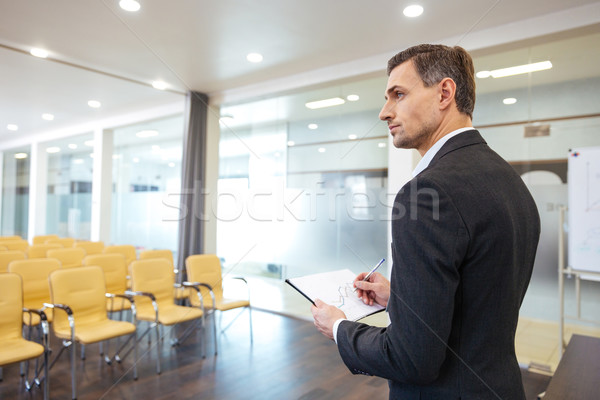 Businessman with clipboard standing in empty conference hall Stock photo © deandrobot