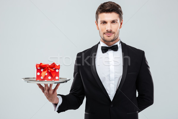 Waiter in tuxedo with bowtie holding present box on tray Stock photo © deandrobot