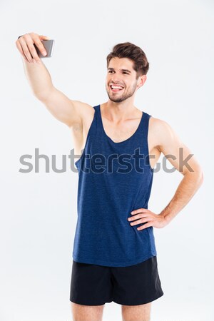 Smiling young sportsman standing and talking selfie with cell phone Stock photo © deandrobot