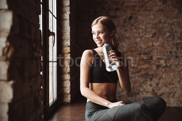 Happy fitness woman drinking water and look aside. Stock photo © deandrobot