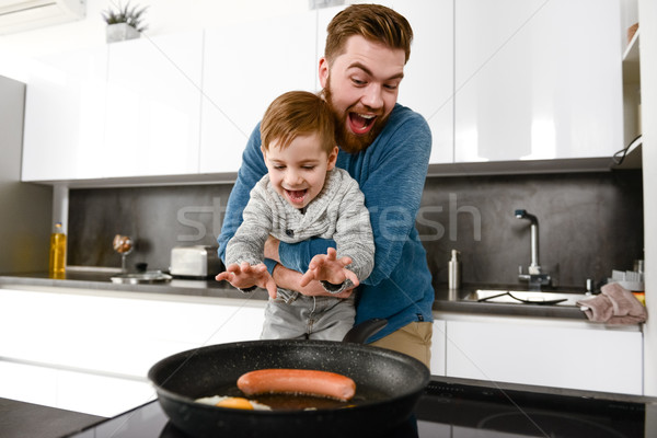 Cheerful bearded father cooking at kitchen with his little son Stock photo © deandrobot