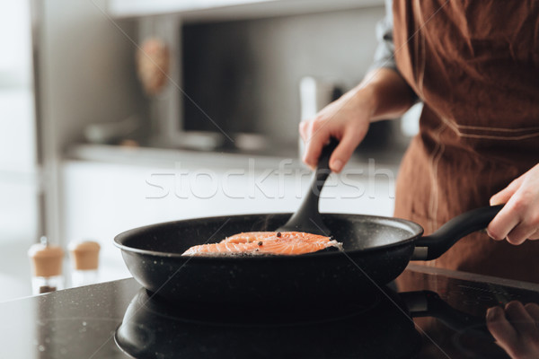 Cropped image of young lady cooking fish. Stock photo © deandrobot