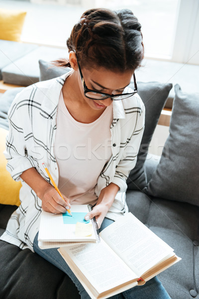 Young amazing african lady wearing glasses sitting in library Stock photo © deandrobot