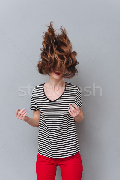 Happy young lady standing over grey wall shaking hair. Stock photo © deandrobot