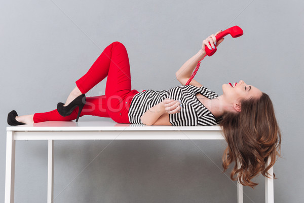 Happy young lady lies on table talking by phone Stock photo © deandrobot