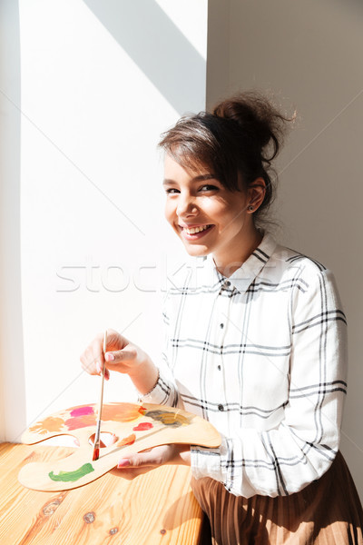 Smiling young woman artist holding palette and looking at camera Stock photo © deandrobot
