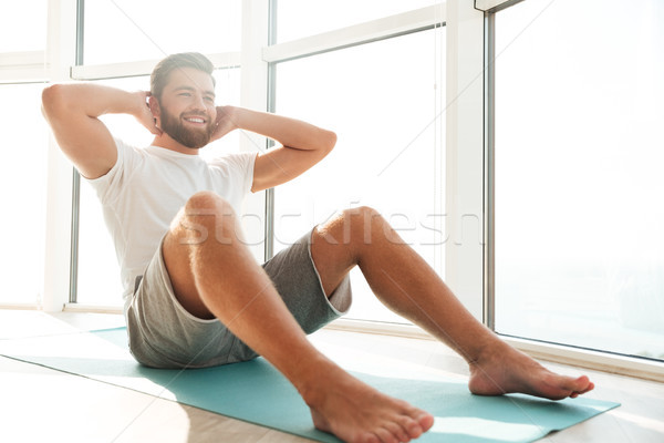 Smiling Handsome bearded man doing abdominals exercises near the window Stock photo © deandrobot