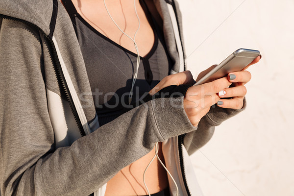 Cropped photo of young woman in sport wear holding mobile phone, Stock photo © deandrobot