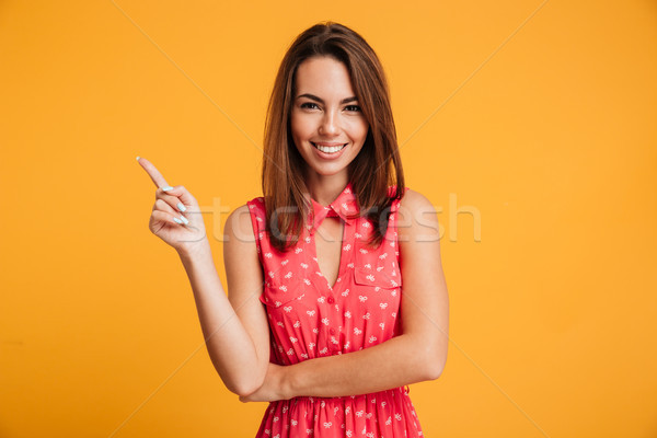 Smiling brunette woman in dress winks and pointing up Stock photo © deandrobot