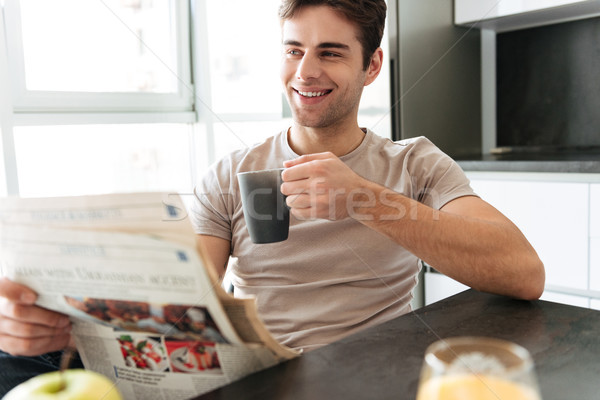 Handsome smiling man with cup of tea reading newspaper in kitchen Stock photo © deandrobot