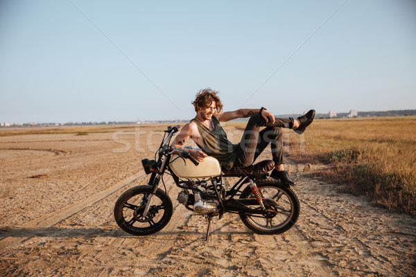 Young brutal man laying on his motorcycle and posing Stock photo © deandrobot