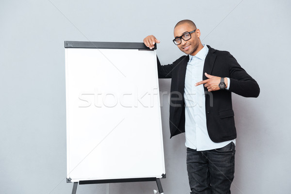Happy african young man standing and pointing on blank flipchart Stock photo © deandrobot