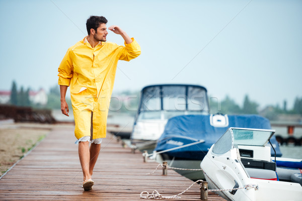 Matróz férfi citromsárga köpeny sétál tenger Stock fotó © deandrobot