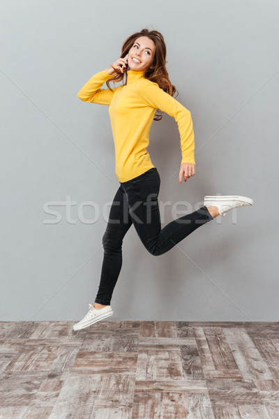 женщину желтый свитер прыжки говорить мобильного телефона Сток-фото © deandrobot