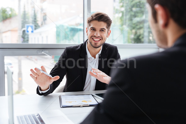 Two happy young businessmen sitting and working on business meeting Stock photo © deandrobot