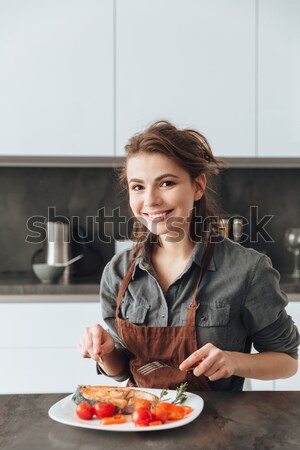 Woman sitting in kitchen while eating fish and tomatoes. Stock photo © deandrobot