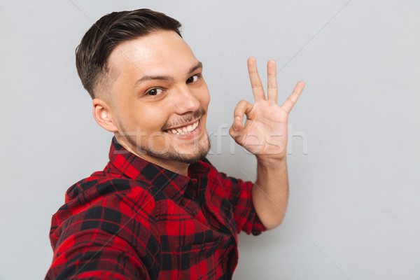 Smiling man standing sideways and showing ok sign Stock photo © deandrobot