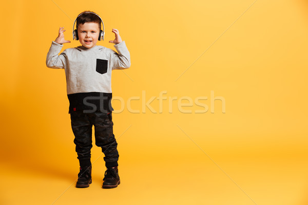 Boy child standing isolated listening music with headphones. Stock photo © deandrobot
