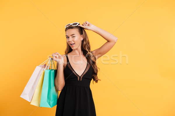 Amazing lady in black dress winking and holding shopping bags. Stock photo © deandrobot