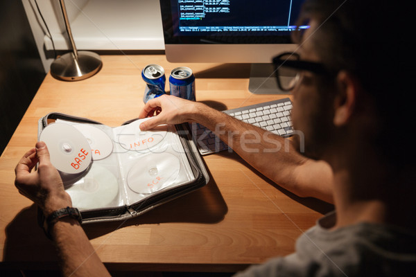 Handsome programmer using computer and choosing CD with data Stock photo © deandrobot