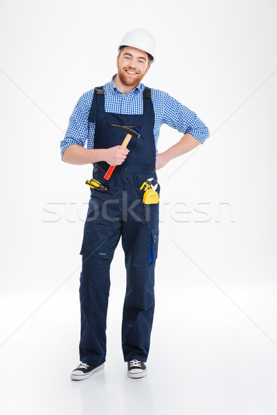 Happy young builder in helmet standing and holding hammer Stock photo © deandrobot