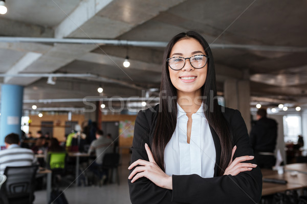 Cheerful asian young businesswoman standing with hands folded in office Stock photo © deandrobot