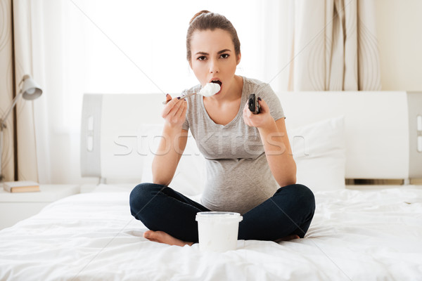 Concentrated pregnant woman with ice cream watching TV on bed Stock photo © deandrobot