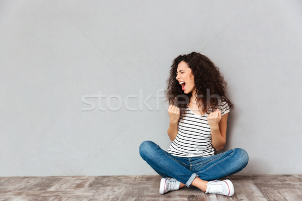 Young curly woman in casual clothes expressing delight while sit Stock photo © deandrobot