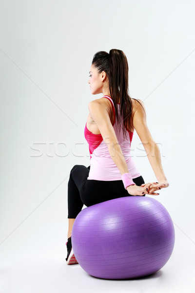 Back view of a young sport woman stretching on fitball on gray background Stock photo © deandrobot