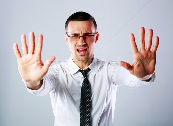 Dissatisfied businessman gesturing stop sign with both hands on gray background Stock photo © deandrobot