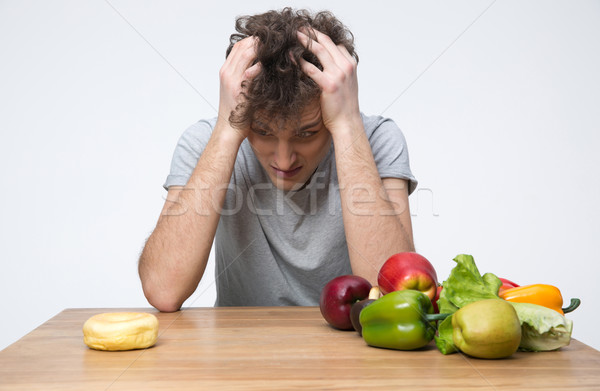 Pensive man sitting at the table with vegetables and donut Stock photo © deandrobot