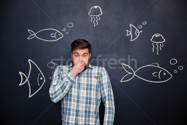 Amusing man closed nose and standing over chalkboard with fishes  Stock photo © deandrobot