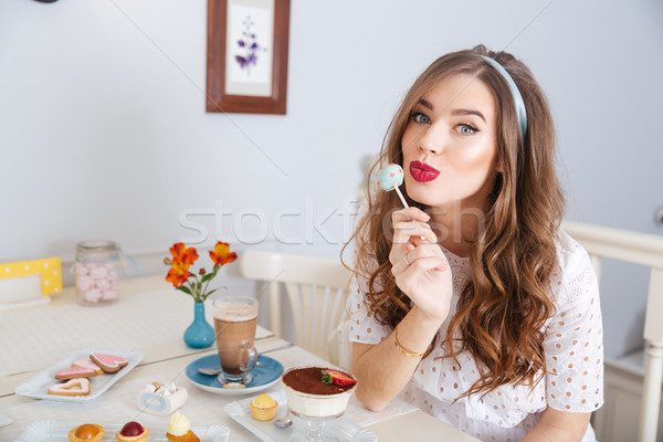 Cute lovely young woman sitting in cafe and eating lollipop  Stock photo © deandrobot