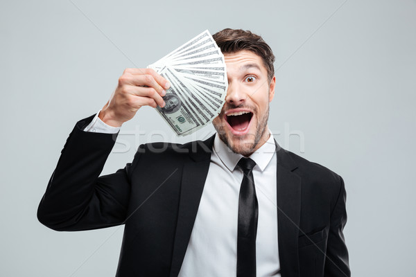 Funny excited young businessman covered one eye with money Stock photo © deandrobot