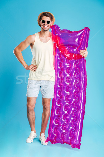 Cheerful man in hat and sunglasses holding pink inflatable mattress Stock photo © deandrobot