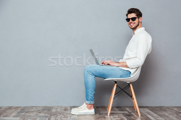Sorridente moço branco camisas óculos de sol usando laptop Foto stock © deandrobot