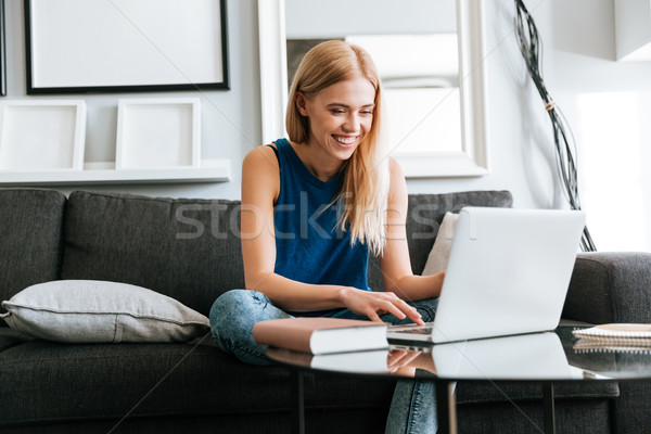 Happy woman sitting on sofa and using laptop at home Stock photo © deandrobot