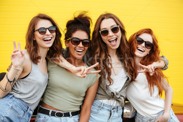 Four young happy women friends standing over yellow wall Stock photo © deandrobot