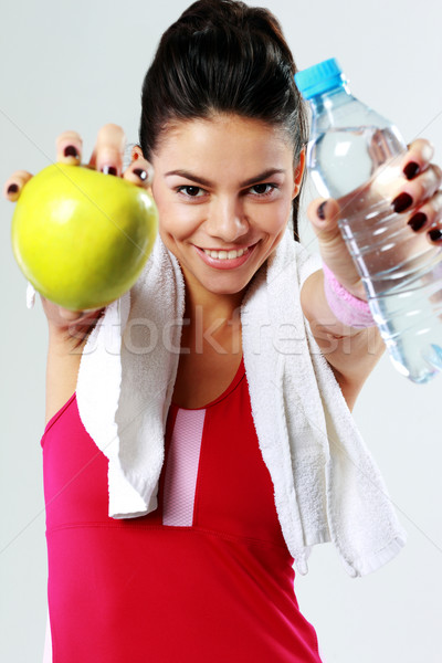 Young smiling sport woman with apple and bottle of water on gray background Stock photo © deandrobot