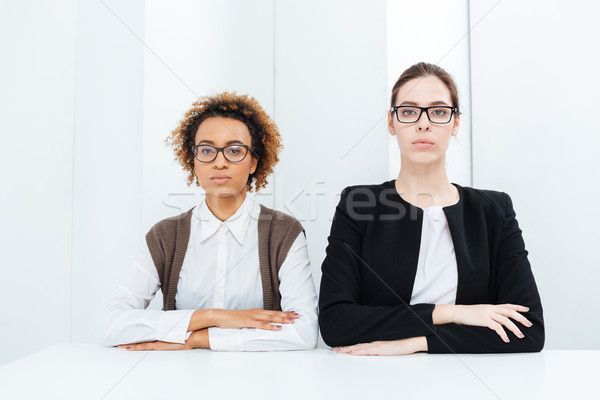 Two serious young busimesswomen in glasses sitting straight  Stock photo © deandrobot
