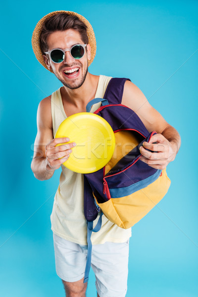 Cheerful young man taking frisbee disk from backpack Stock photo © deandrobot