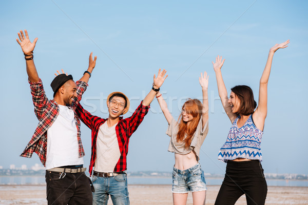 Alegre jovem amigos em pé ao ar livre as mãos levantadas Foto stock © deandrobot