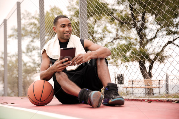 Stock photo: Cheerful african basketball player sitting inpark and holding ta