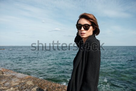 Woman in sunglasses and black coat standing on the seaside Stock photo © deandrobot