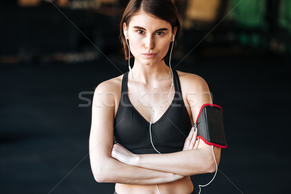 Woman athlete using earphones standing with arms crossed in gym Stock photo © deandrobot