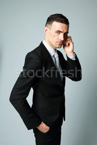 Confident businessman talking on his mobile phone on gray background Stock photo © deandrobot