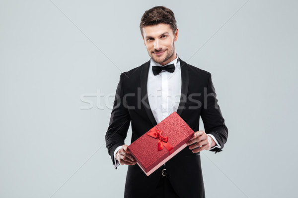 Confident attracive man in tuxedo standing and holding gift box Stock photo © deandrobot